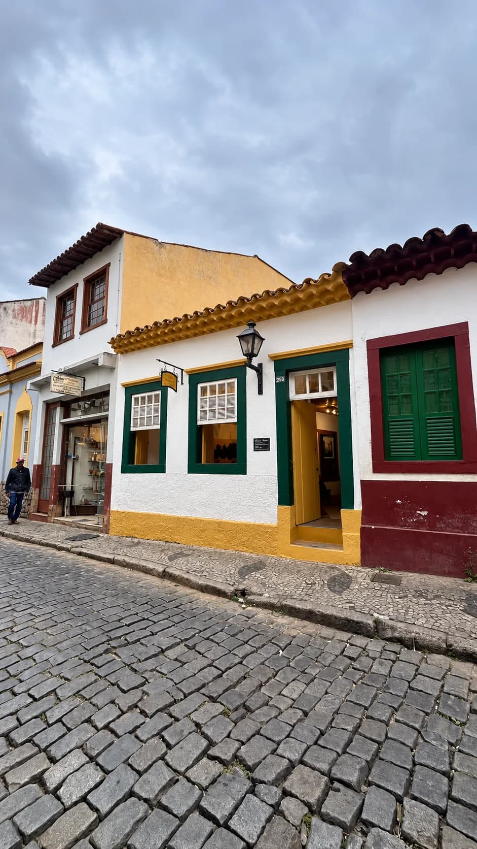 Fachada da loja Wit Molduras & Artes, casa colonial branca e amarela de janelas verdes no Centro de São João del Rei